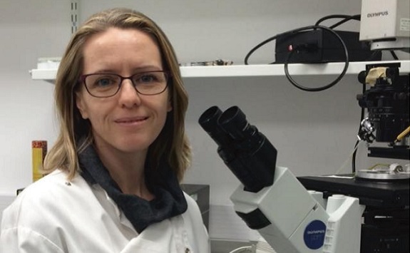 A person wearing a laboratory coat in a white room next to a microscope